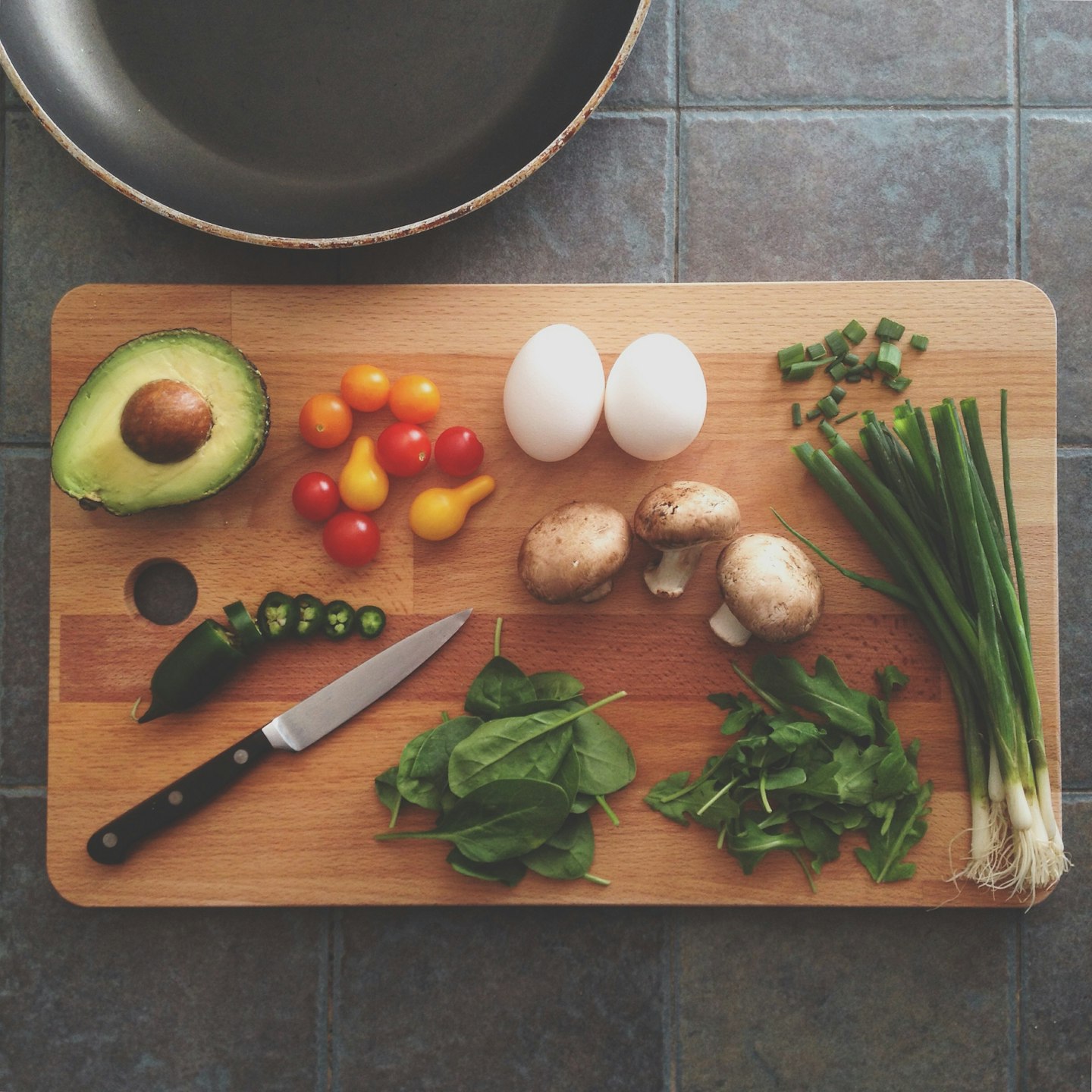 Avocado, Tomaten, Eier, Pilze, Spinat und Frühlingszwiebeln auf einem Holzbrett